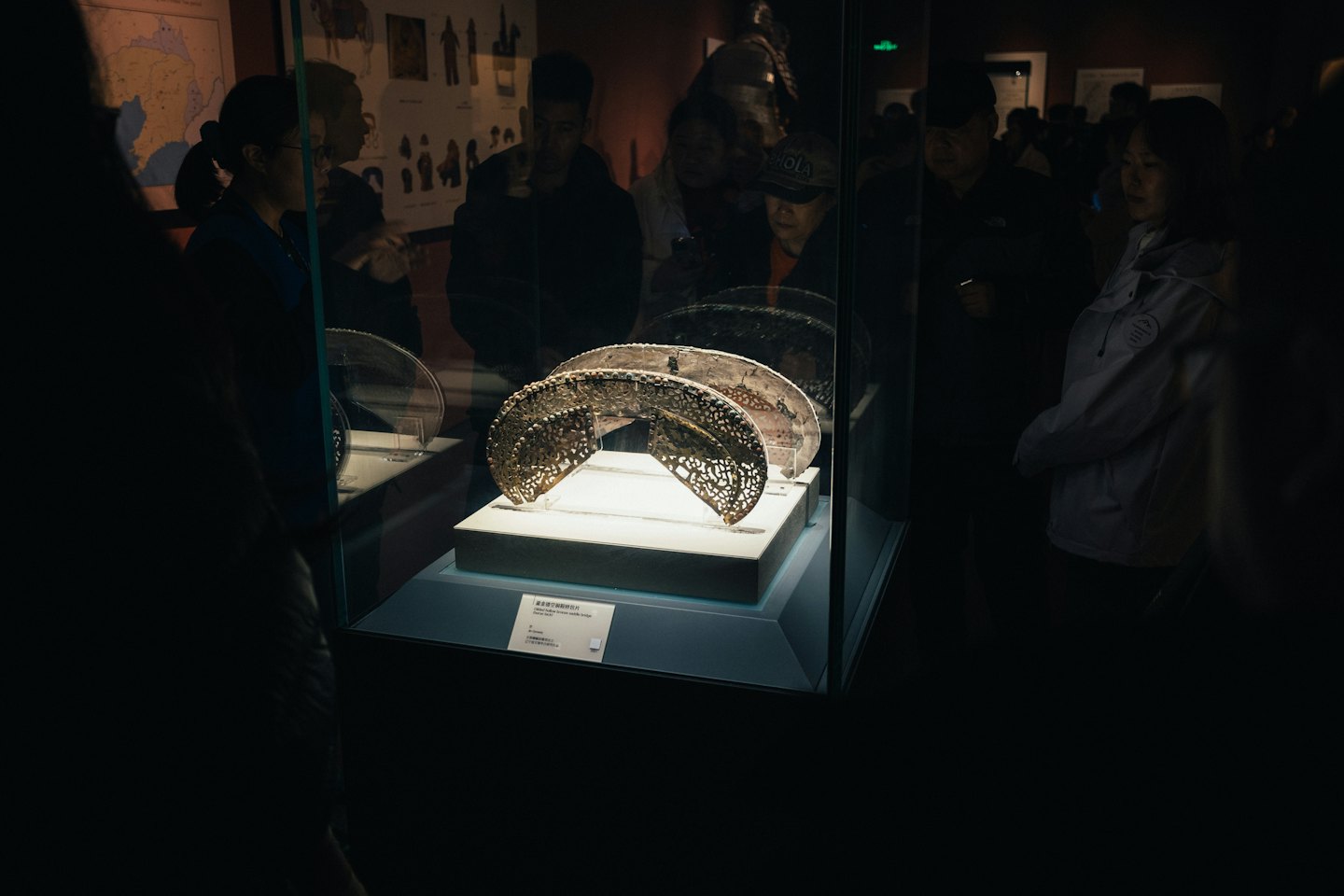 Visitors observe ornate metallic artifacts in a museum display case.