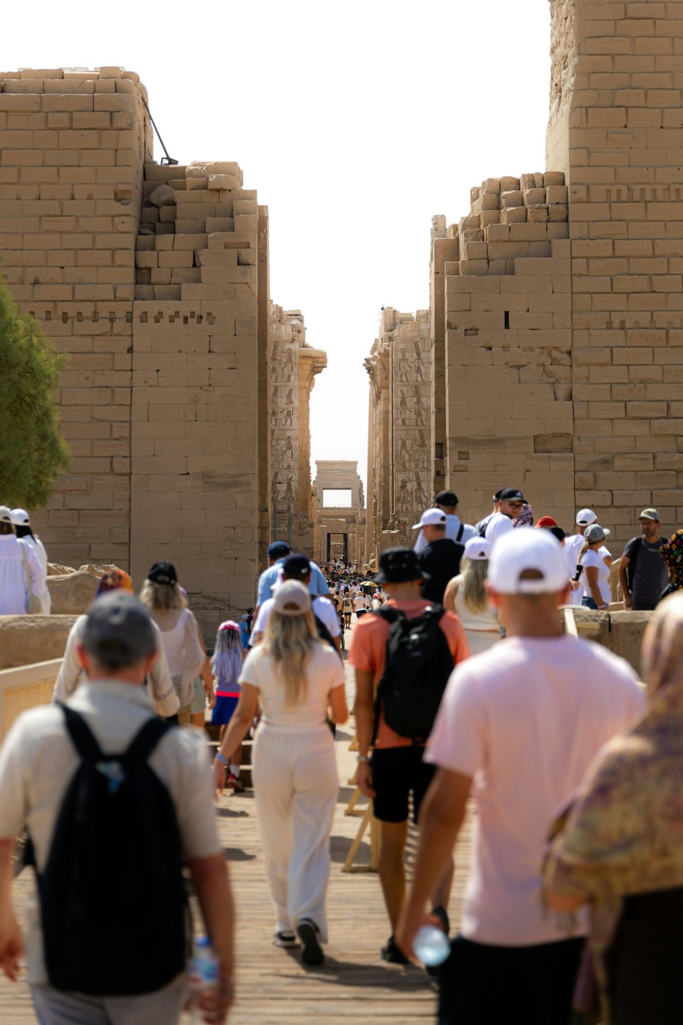 Tourists walk on a wooden path toward an ancient Egyptian temple.