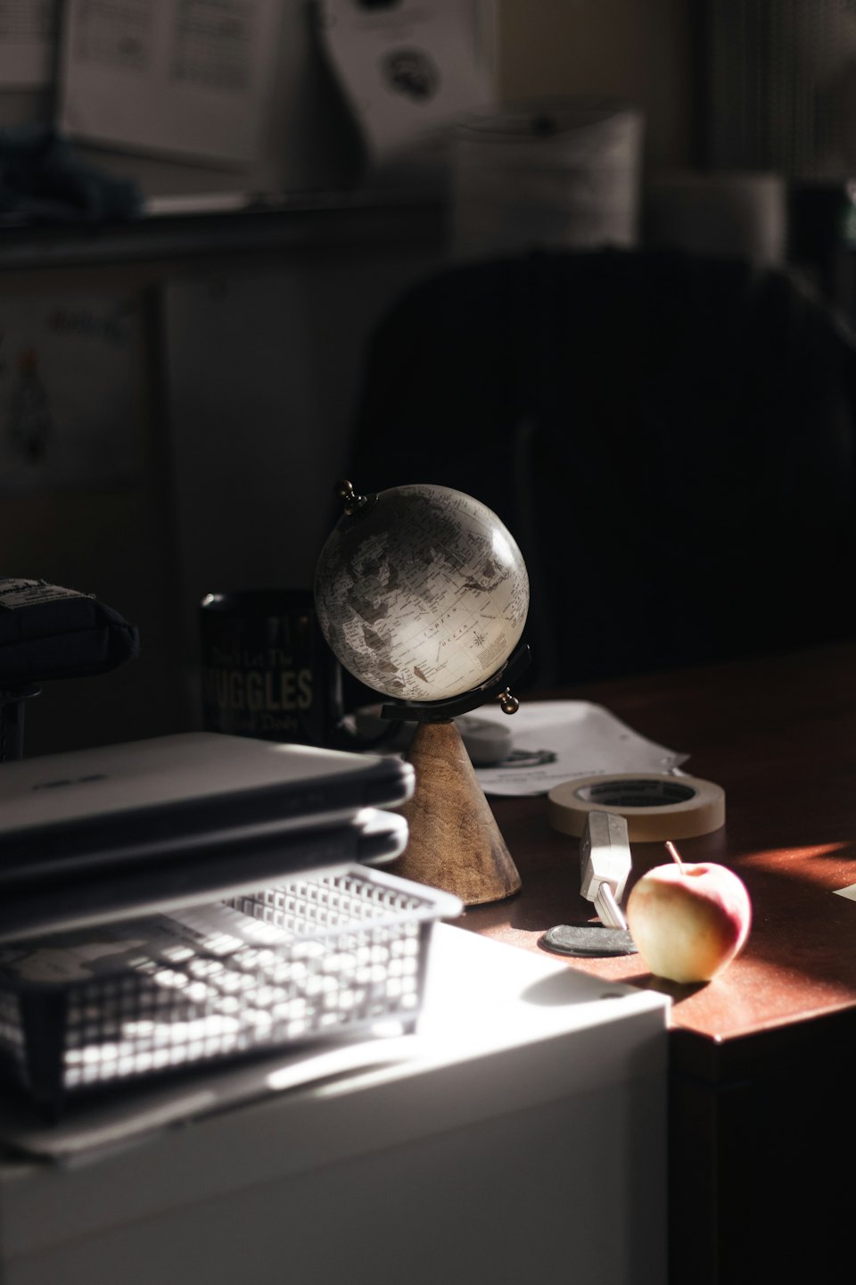 A desktop globe rests on a wooden desk next to a laptop and documents.